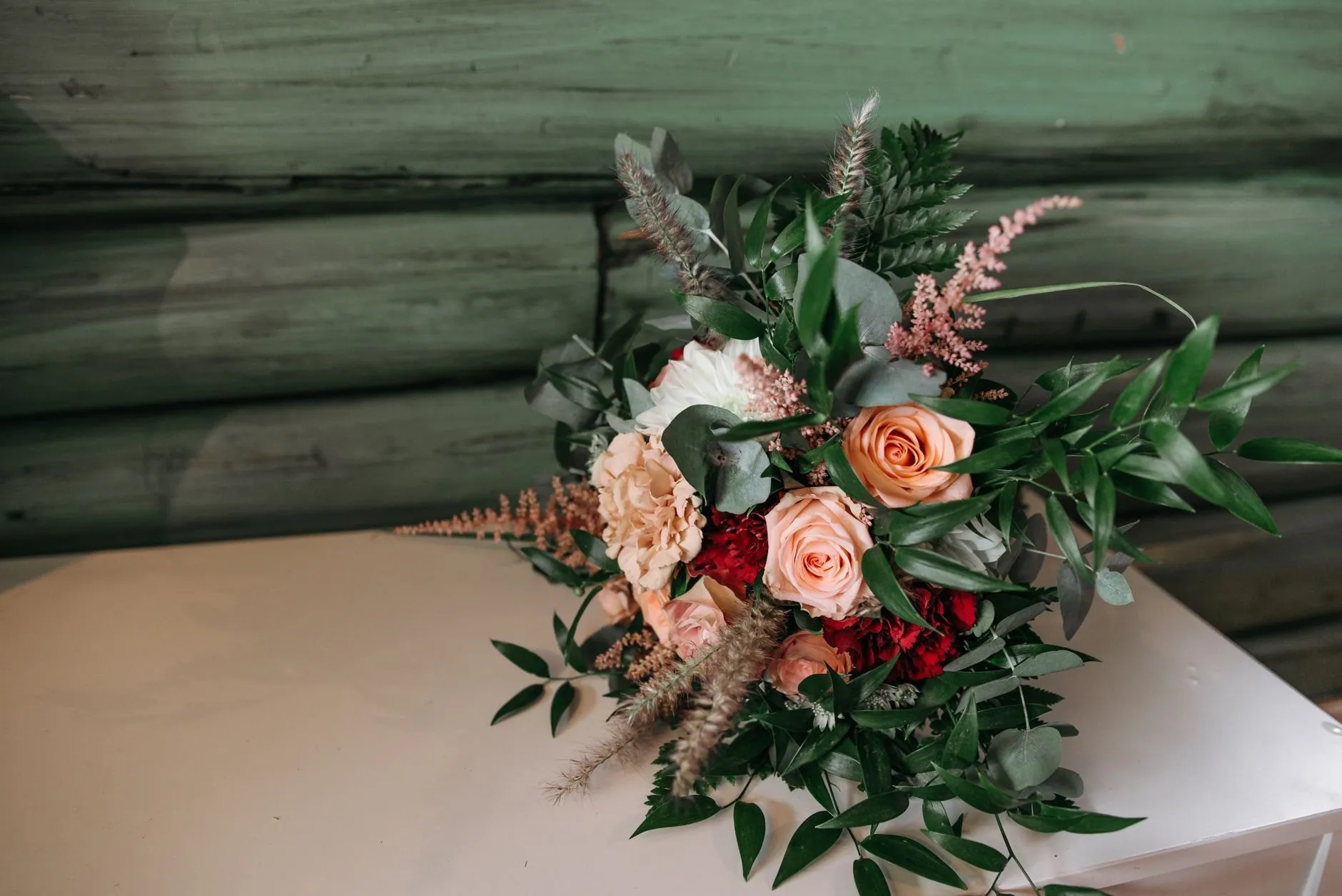 A bridal bouquet of peach roses, astilbe and greenery resting on a white bench