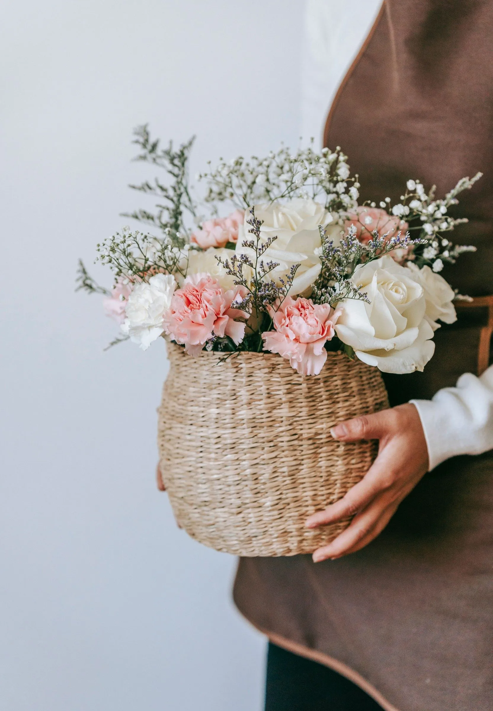 A seagrass basket of white roses, pink carnations and gypsophila held against a florist's apron