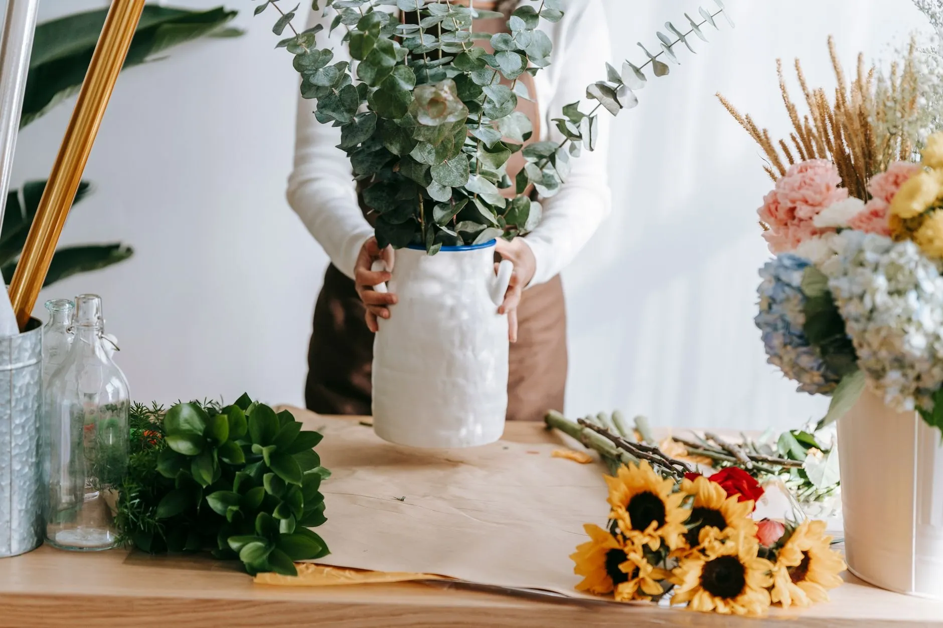 The studio workbench with eucalyptus in a stoneware jug, sunflowers and hydrangea on kraft paper