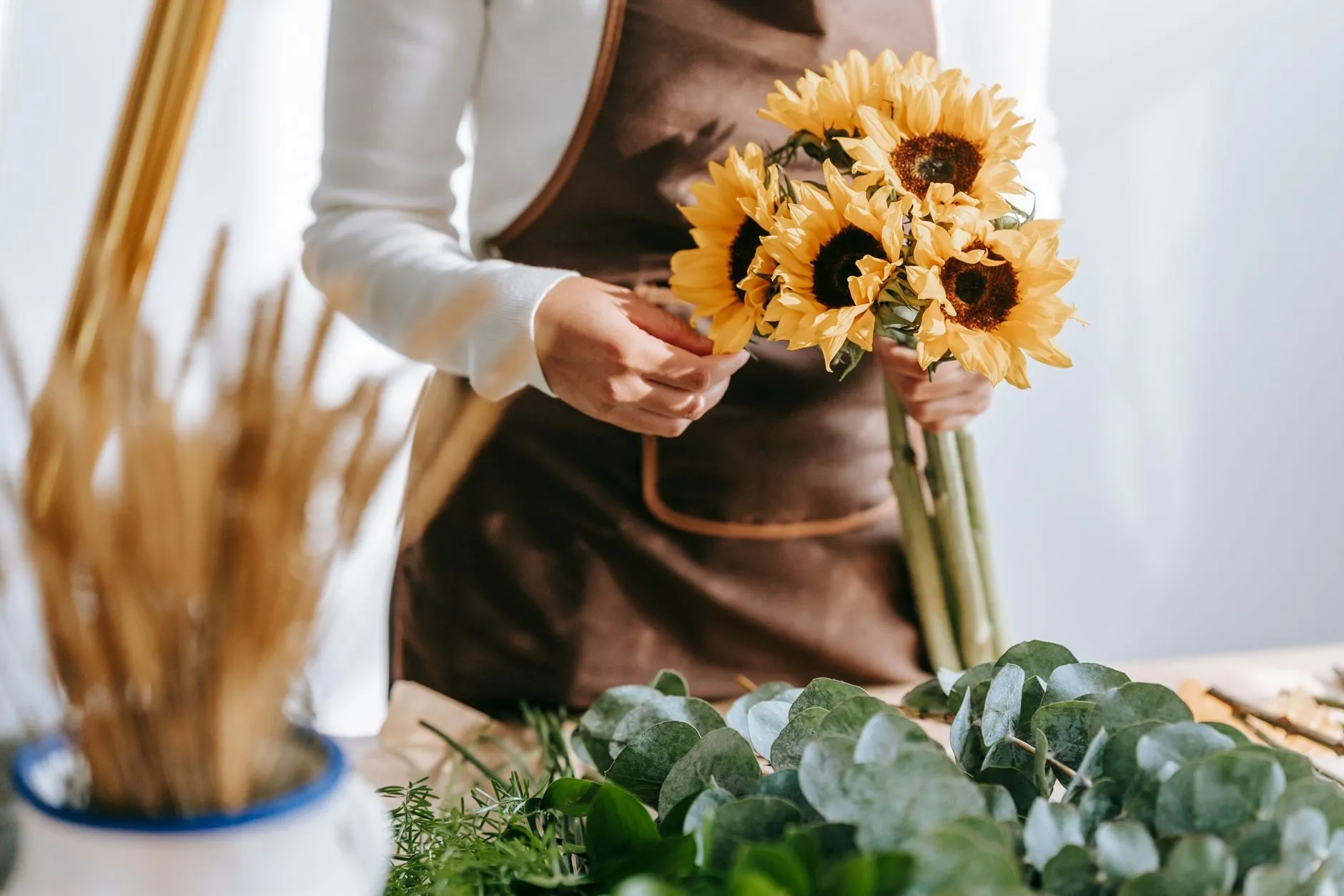 Hands gathering a bunch of sunflowers over a table of eucalyptus