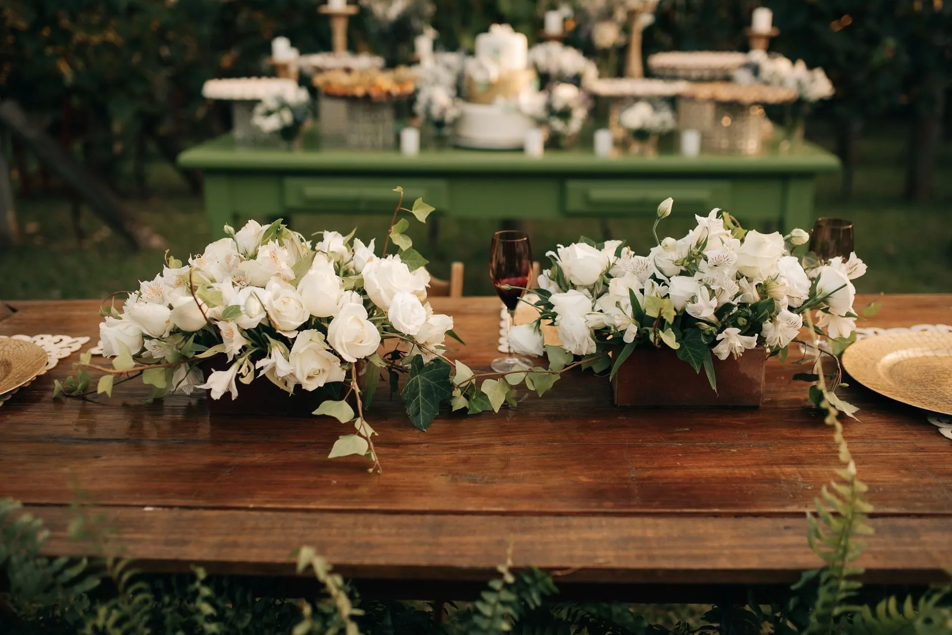 Long low arrangements of white roses along a rustic wooden wedding table